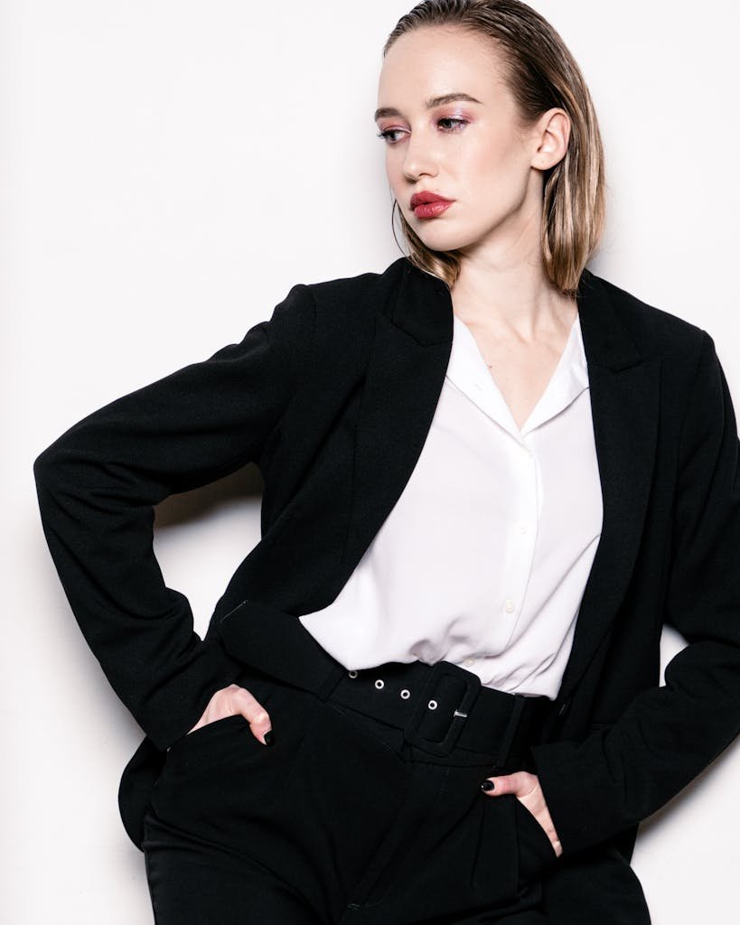 Elegant woman in a black suit posing with hands in pockets on a white background, showcasing corporate style.